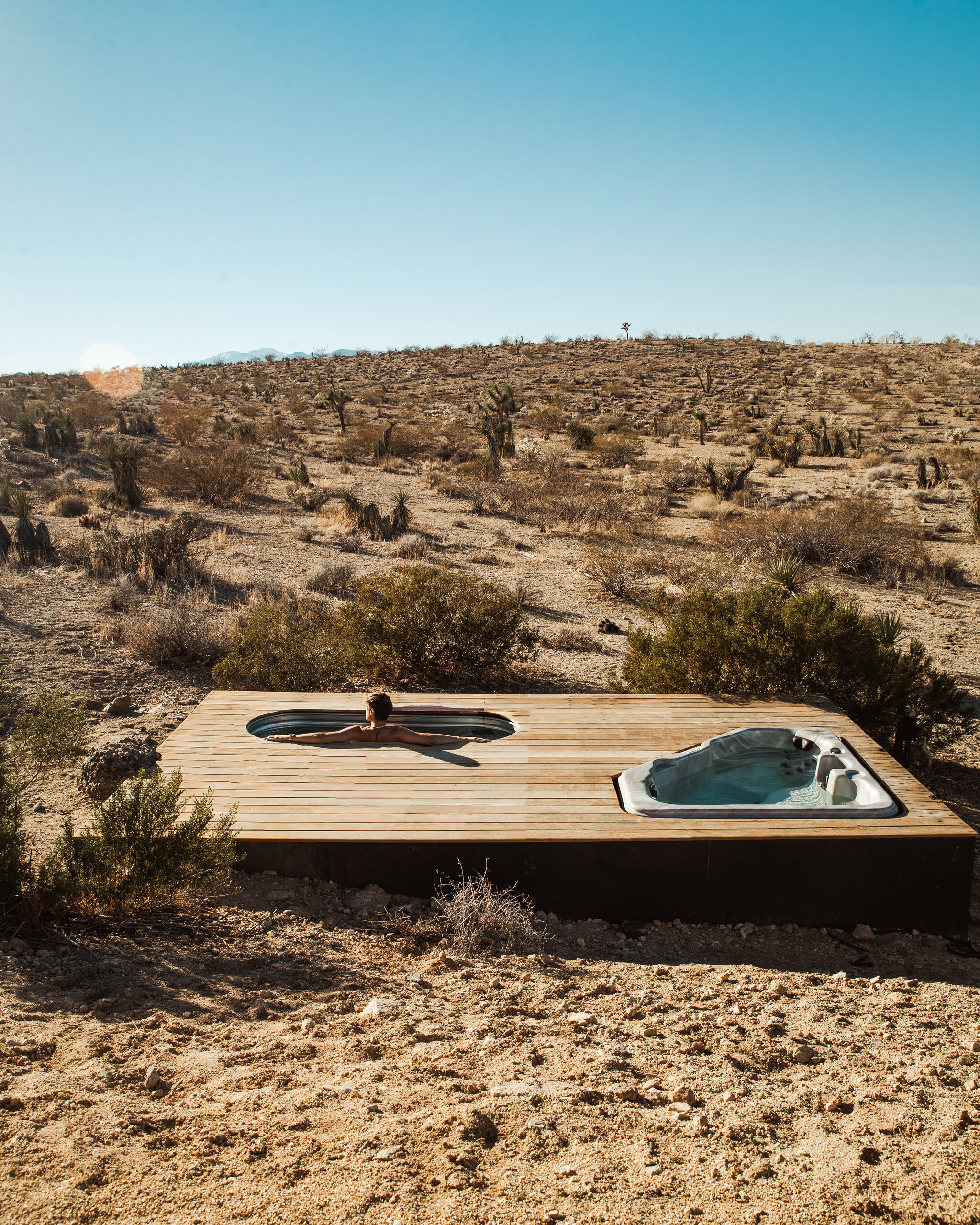 Guest cooling off in the cowboy tub at Pause House under a midday blue sky